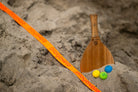 Teak Vole Paddle in the sand with laser logo and Rubber Vole Drops next to the Rally Court on the beach